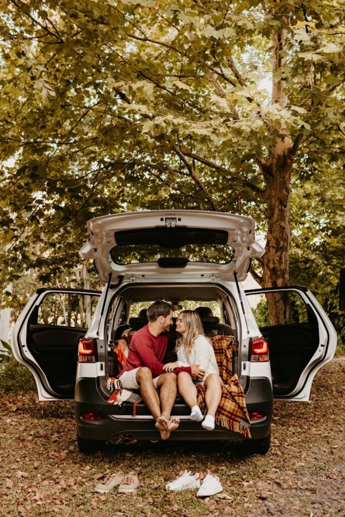 Couple sitting in the back of a car, sharing a romantic moment outdoors among lush trees.
